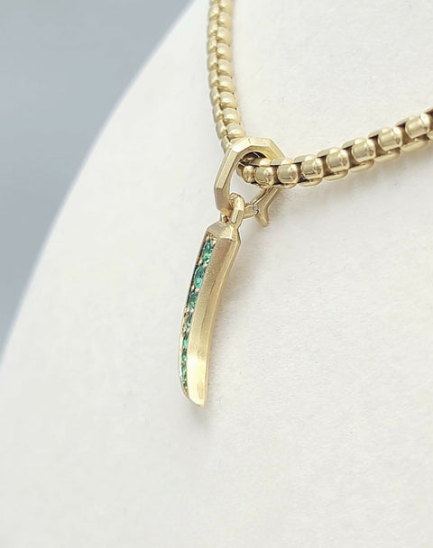 A gold chain necklace with a claw-shaped pendant featuring a vertical inlay of green stones, displayed on a white jewelry bust.