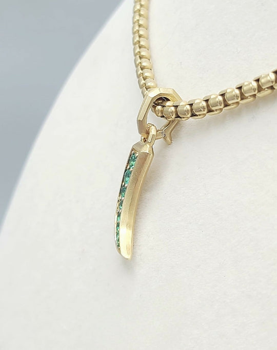 A gold chain necklace with a claw-shaped pendant featuring a vertical inlay of green stones, displayed on a white jewelry bust.