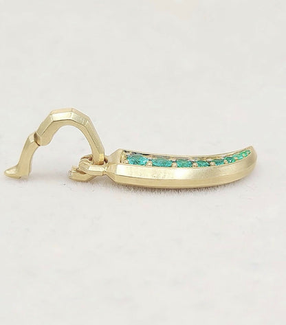 A gold-toned curved earring with a row of small green stones set along the front, photographed on a plain light background.