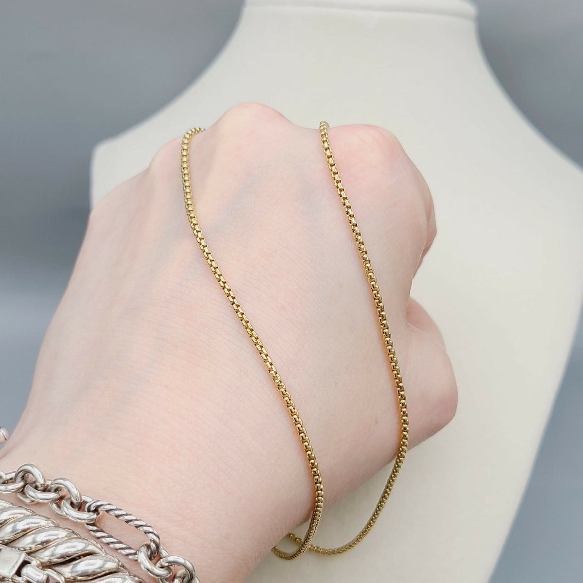 Gold chain necklace being worn on a hand with a neutral background