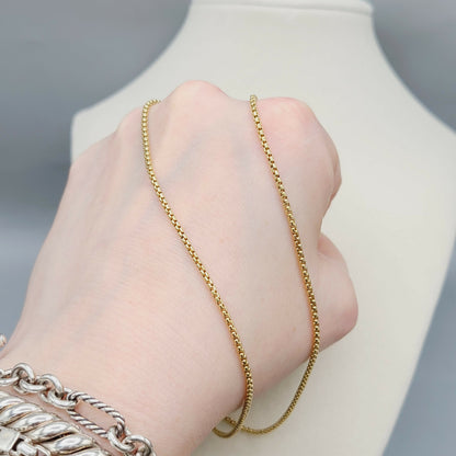 Gold chain necklace being worn on a hand with a neutral background