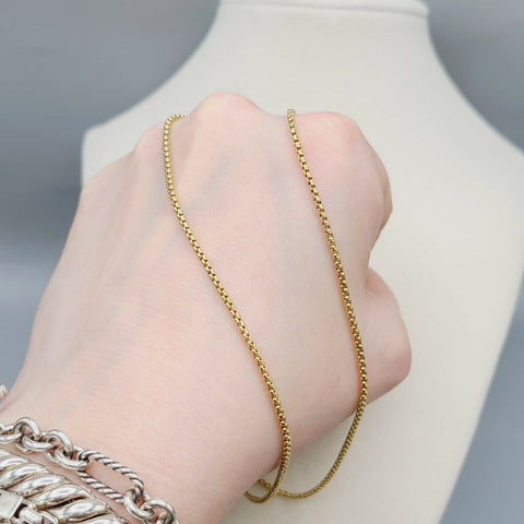 Gold chain necklace being worn on a hand with a neutral background