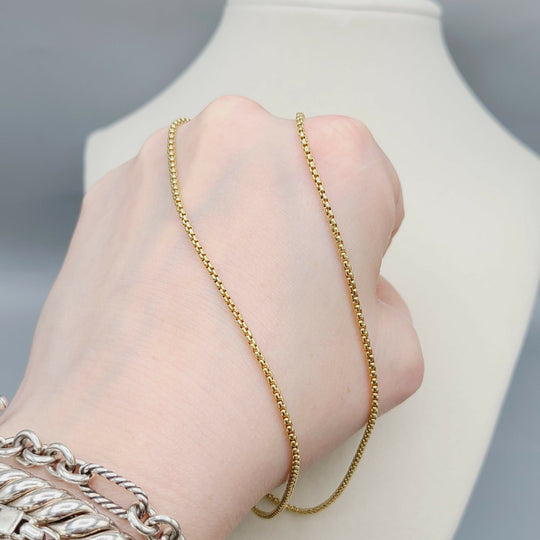 Gold chain necklace being worn on a hand with a neutral background
