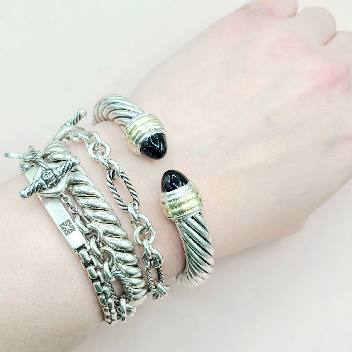 Silver bracelets with charms on a wrist against a light background