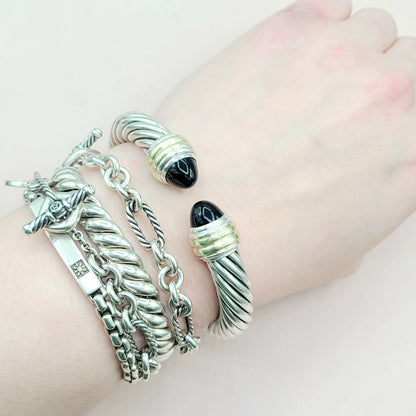 Silver bracelets with charms on a wrist against a light background