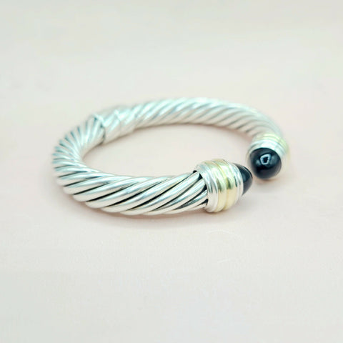 Silver cable-style bracelet with a black bead on a light pink background