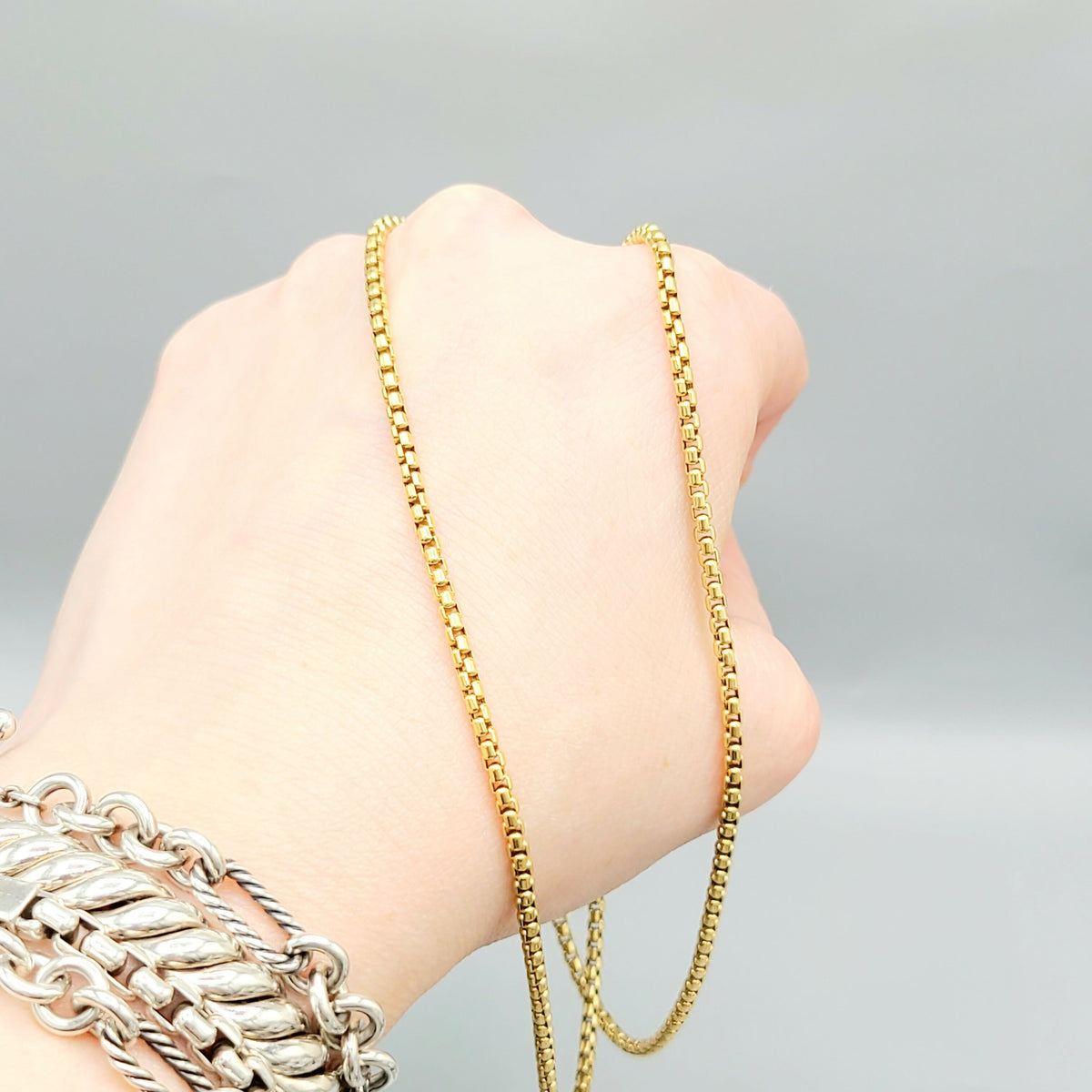 Gold chain necklace being worn on a wrist with a gray background