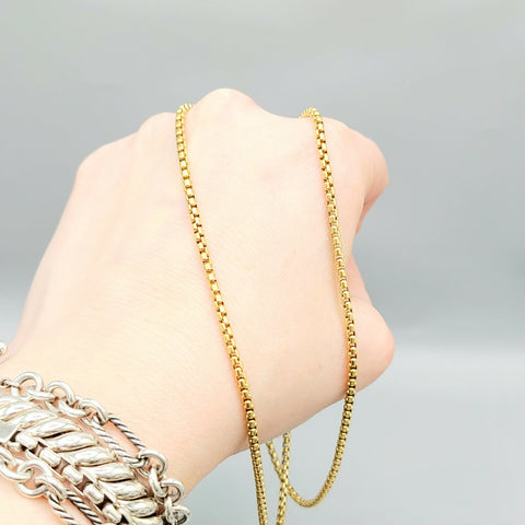 Gold chain necklace being worn on a wrist with a gray background