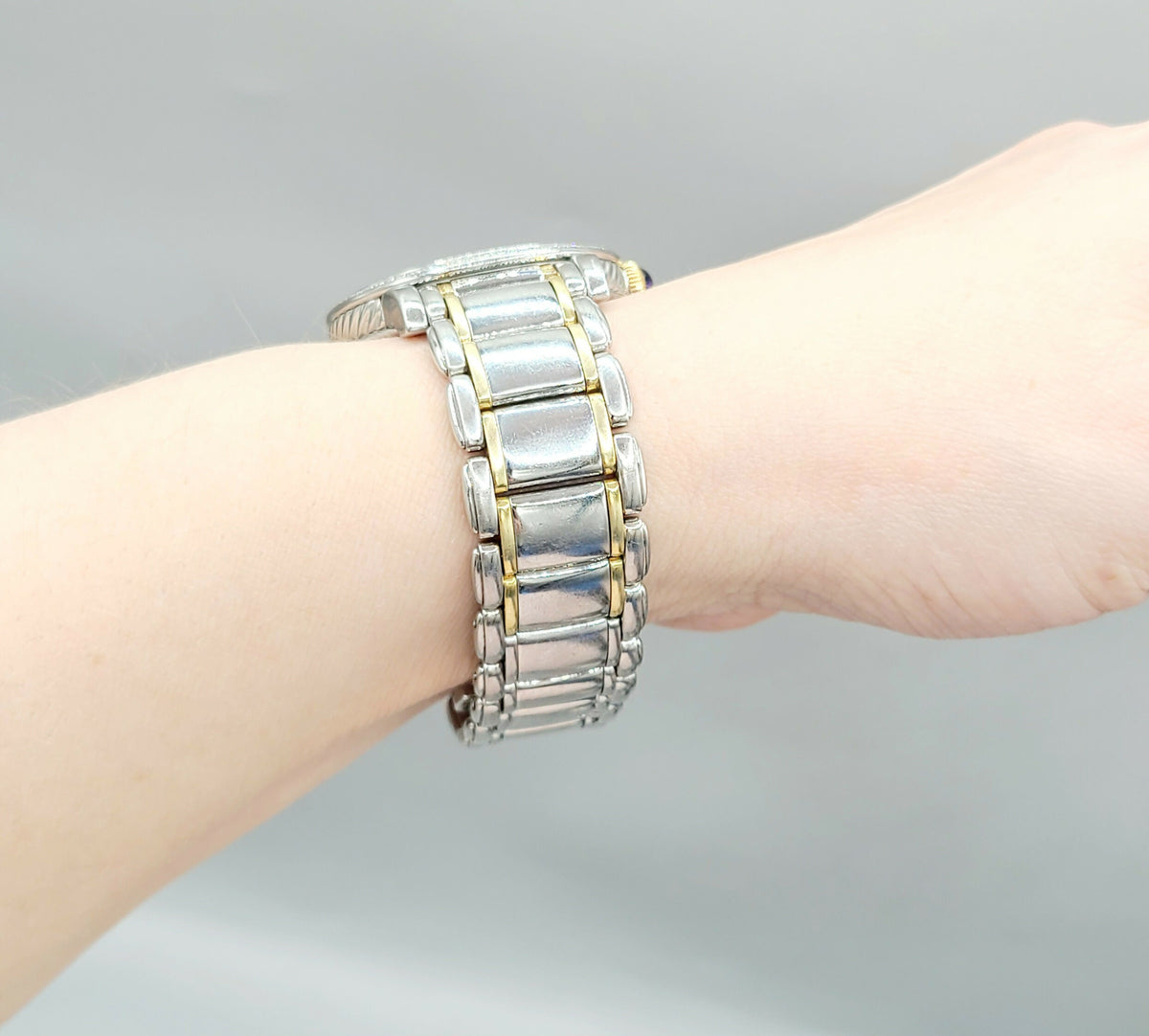 Silver bracelet with gold accents on a wrist against a gray background