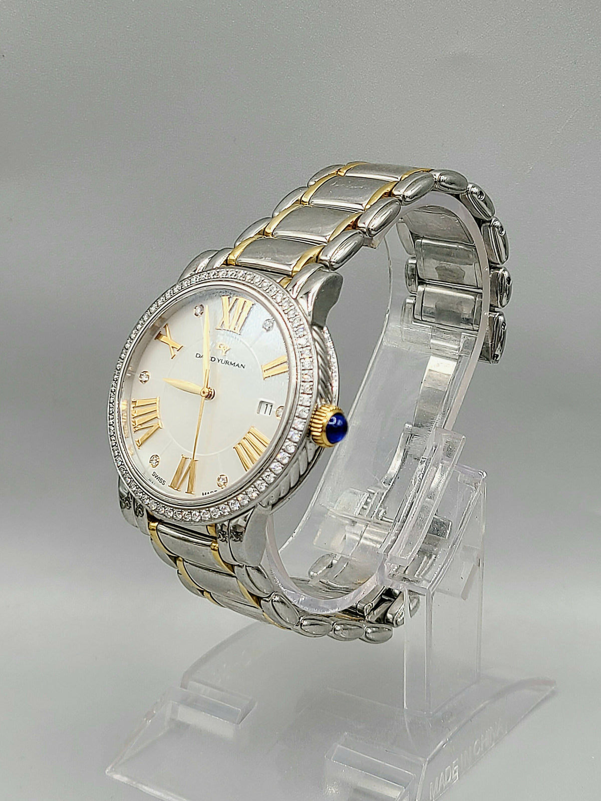 Silver and gold watch on a clear stand with a gray background