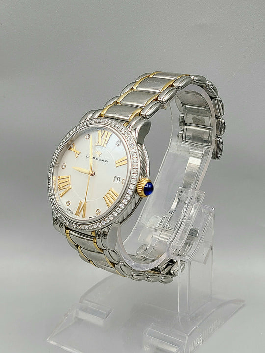 Silver and gold watch on a clear stand with a gray background