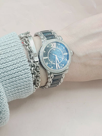 Silver watch with blue face on a wrist, wearing a light blue sweater.
