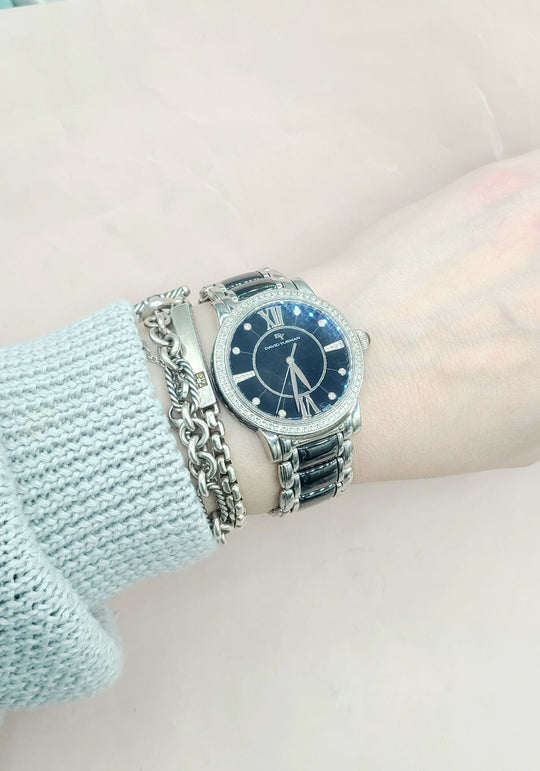 Wrist wearing a silver watch with a blue face on a light background