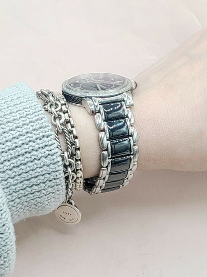 Close-up of a wrist wearing a silver watch with multiple bracelets on a light pink background