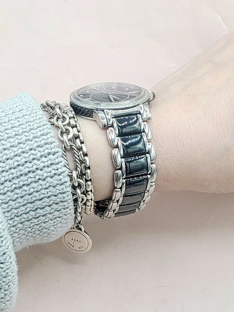 Close-up of a wrist wearing a silver watch with multiple bracelets on a light pink background