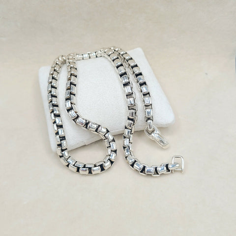 A silver-toned box chain necklace with clear rectangular crystals, draped over a white display cushion on a light beige background.