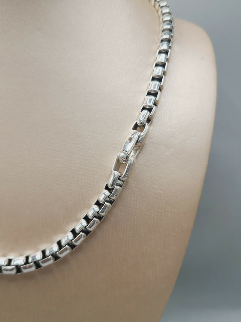 A silver box chain necklace displayed on a beige mannequin bust against a soft gray background.