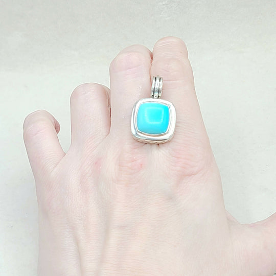 Turquoise stone pendant on a silver chain held in a hand against a white background