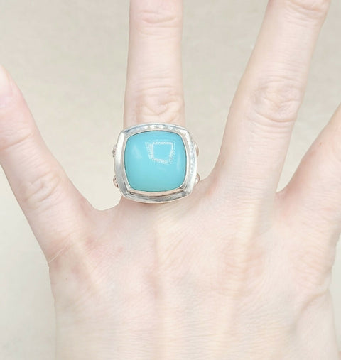 Turquoise ring with silver band on a hand against a light background