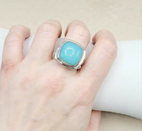 Turquoise ring with silver band on a hand against a neutral background