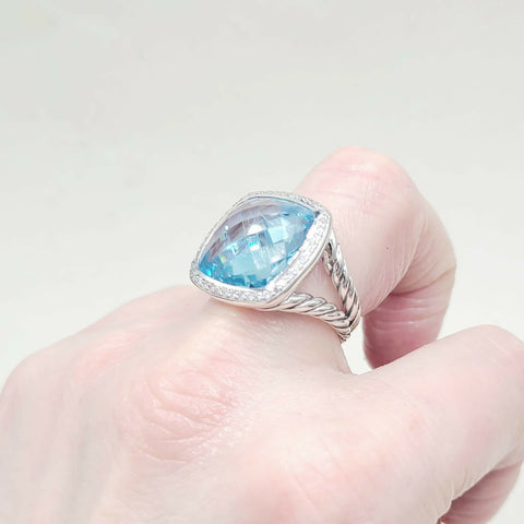 Silver ring with a blue gemstone held in a hand against a light background