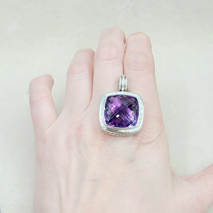 Hand wearing a silver ring with a purple gemstone on a light background