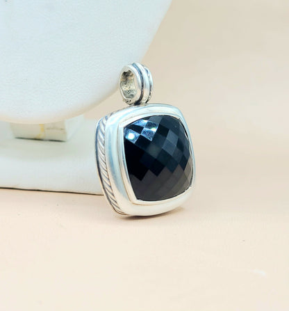 Silver pendant with a black stone on a beige surface