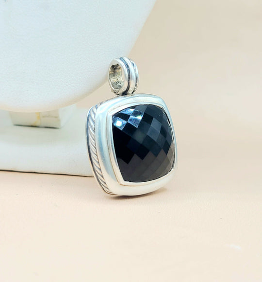 Silver pendant with a black stone on a beige surface