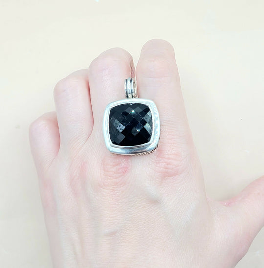 Black stone pendant on a silver chain held in a hand against a light background