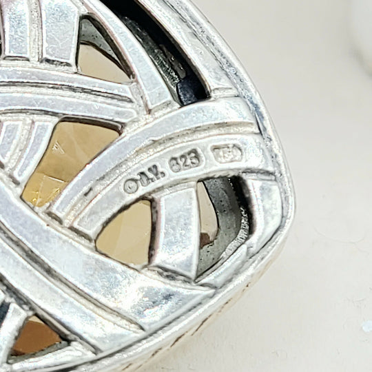Close-up of a silver ring with intricate design and '925' stamp on a light background