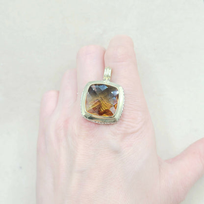 Gold pendant with a gemstone held on a hand against a light background