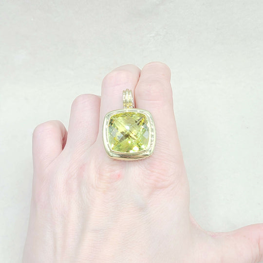 Gold pendant with a yellow gemstone held in a hand against a light background