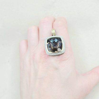 Gold pendant with a dark gemstone held in a hand against a light background