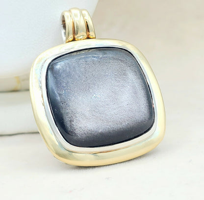 Gold pendant with a dark gray stone on a light background