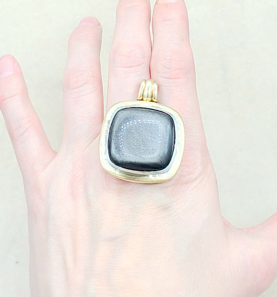 Gold pendant with a gray stone held in a hand against a white background