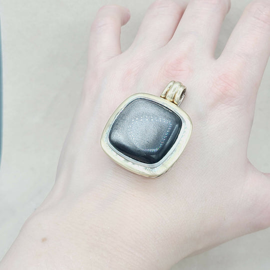 Gold pendant with a black stone held in a hand against a neutral background