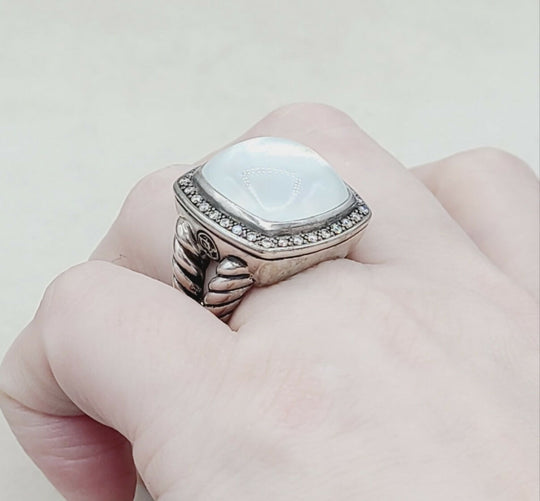 Silver ring with a large stone on a finger against a white background