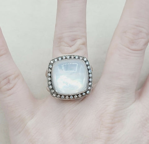 Ring with a large square gemstone and diamond accents on a hand against a neutral background