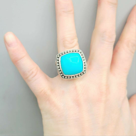 Turquoise ring with silver band on a hand against a gray background