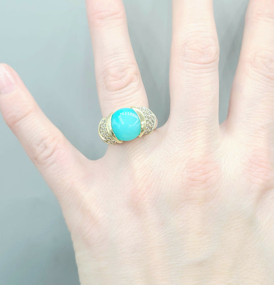 Turquoise ring with gold accents on a hand against a light gray background
