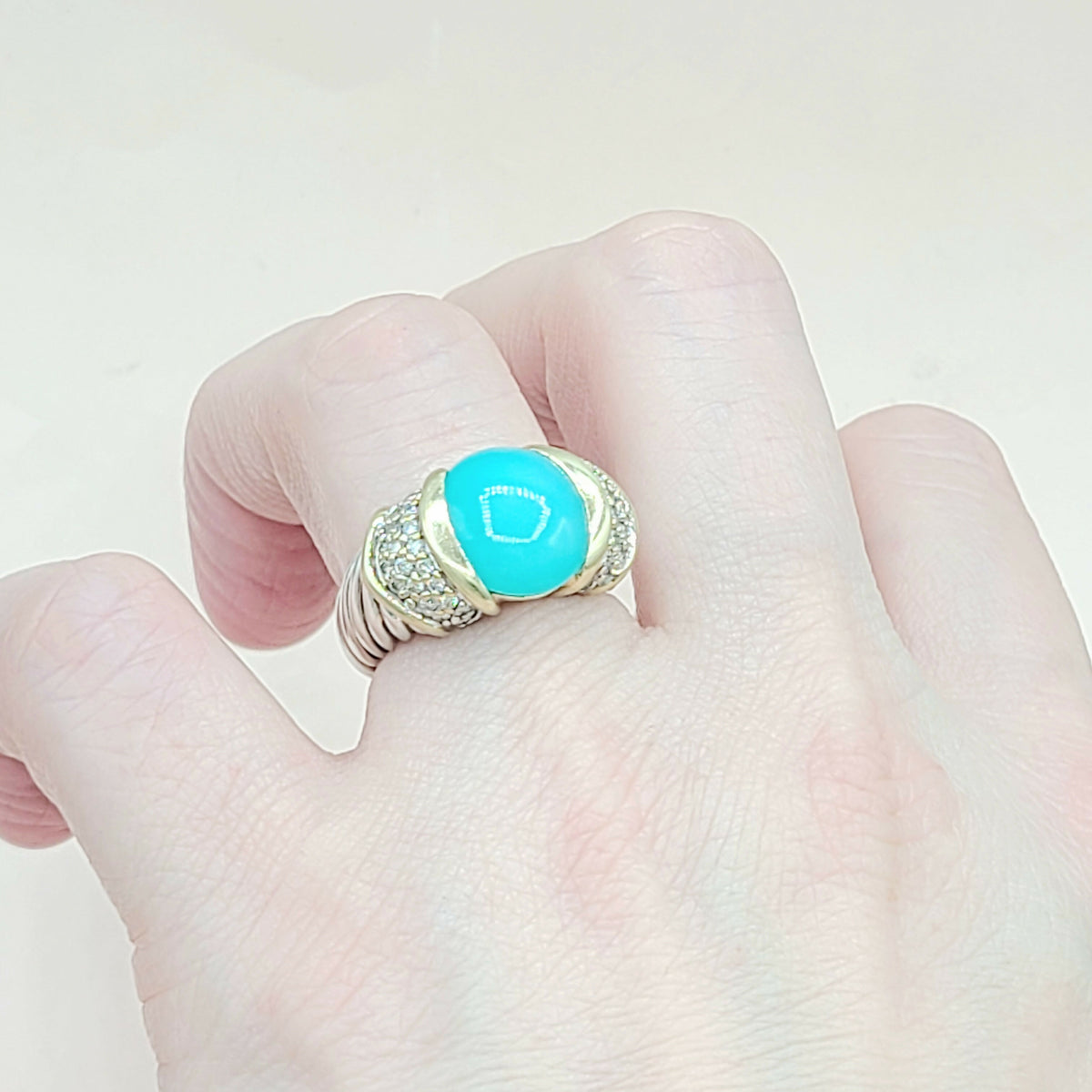 Turquoise ring with gold accents on a finger against a light background