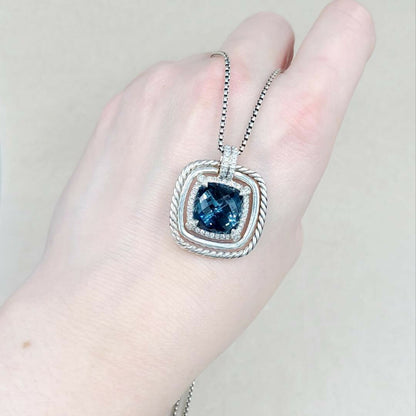 Silver necklace with a blue gemstone pendant held in a hand against a neutral background