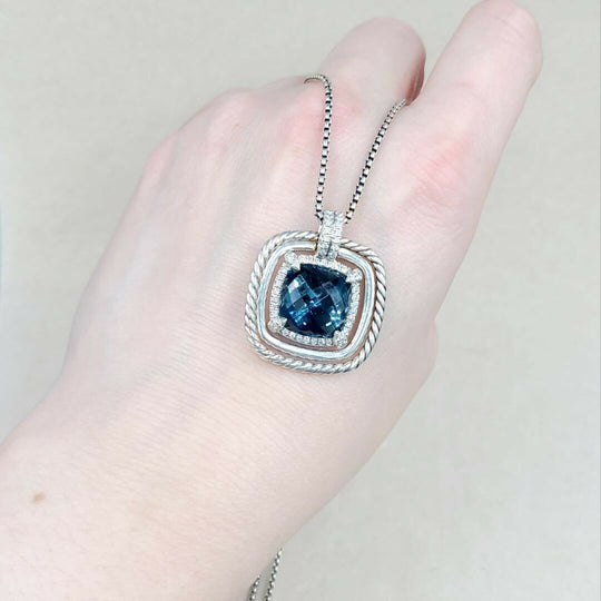 Silver necklace with a blue gemstone pendant held in a hand against a neutral background
