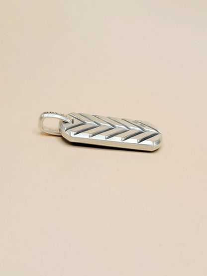 A silver chevron-patterned pendant with a small loop at the top, shown on a plain beige background.
