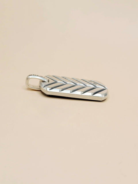 A silver chevron-patterned pendant with a small loop at the top, shown on a plain beige background.