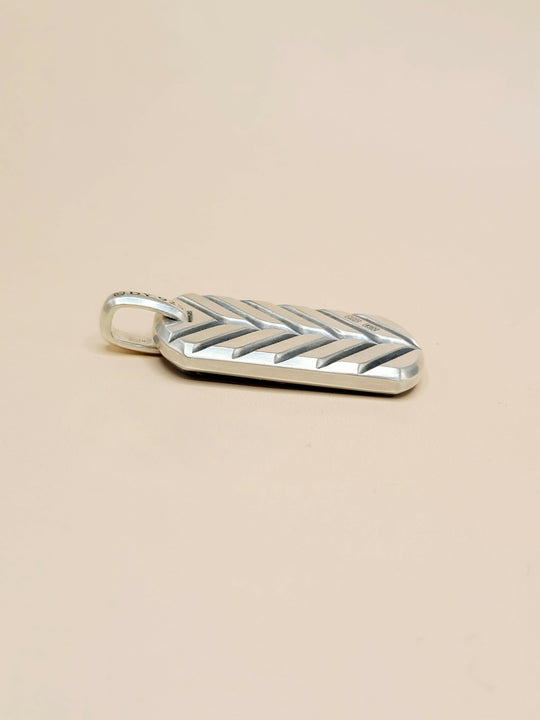 A silver chevron-patterned pendant with a small loop at the top, shown on a plain beige background.