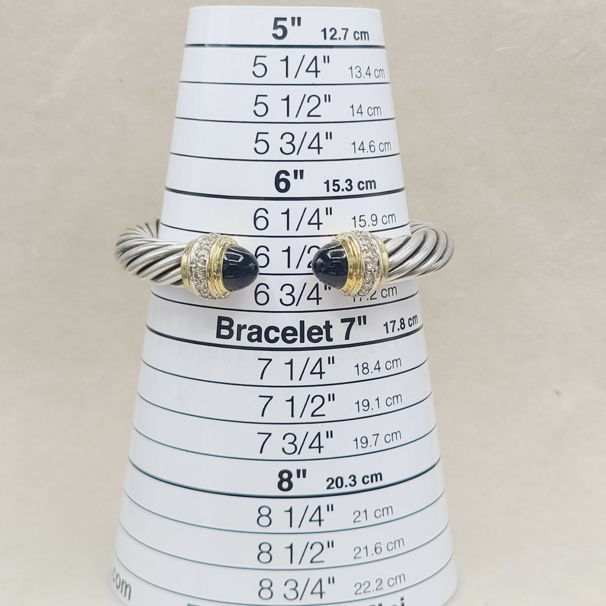 A silver-toned twisted rope bracelet with black onyx stone accents and small clear stones, displayed on a white cone-shaped sizing ruler for bracelets.