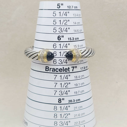 A silver-toned twisted rope bracelet with black onyx stone accents and small clear stones, displayed on a white cone-shaped sizing ruler for bracelets.