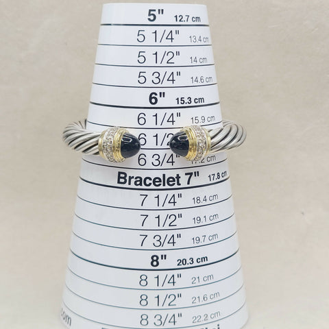 A silver-toned twisted rope bracelet with black onyx stone accents and small clear stones, displayed on a white cone-shaped sizing ruler for bracelets.