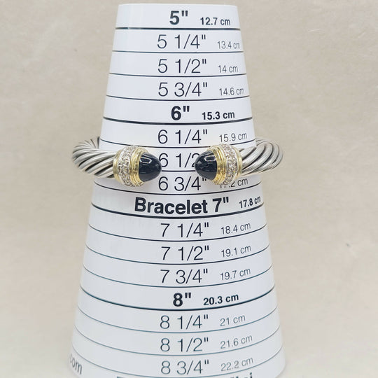 A silver-toned twisted rope bracelet with black onyx stone accents and small clear stones, displayed on a white cone-shaped sizing ruler for bracelets.